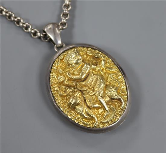 An Indian white and yellow metal oval locket embossed with a deity, on a white metal chain, locket 5cm.